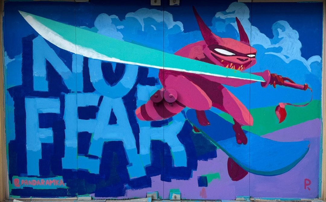 Magenta horned creature on a skateboard swinging a mint sword beside the words NO FEAR, painted on shop shutters