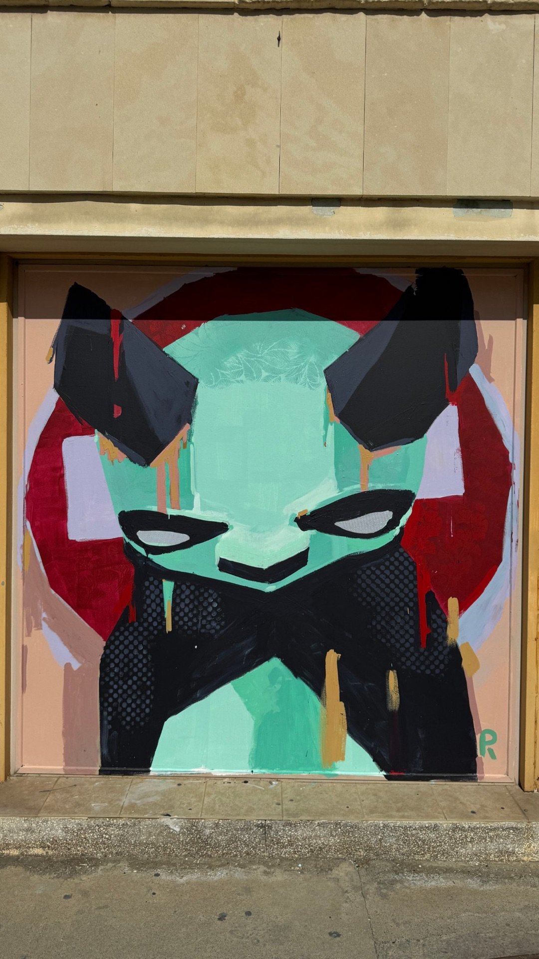 Mint-green horned figure with crossed black arms in front of a red no-entry sign, painted on a garage door